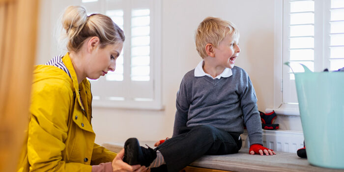 A wide shot of a Caucasian, mother helping her son put his shoes on before school.