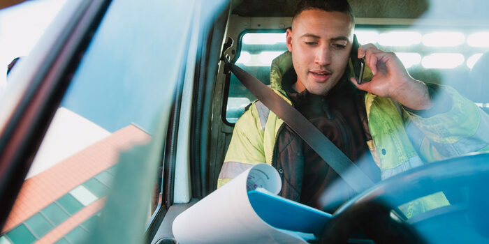 workman-van Mid-adult manual worker is sitting in his van, looking through paperwork while speaking to someone on the phone.